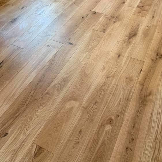Light brown wooden floor with visible grain patterns and small knots, showing long and wide planks arranged parallel to each other. The surface appears clean and smooth with a natural finish.