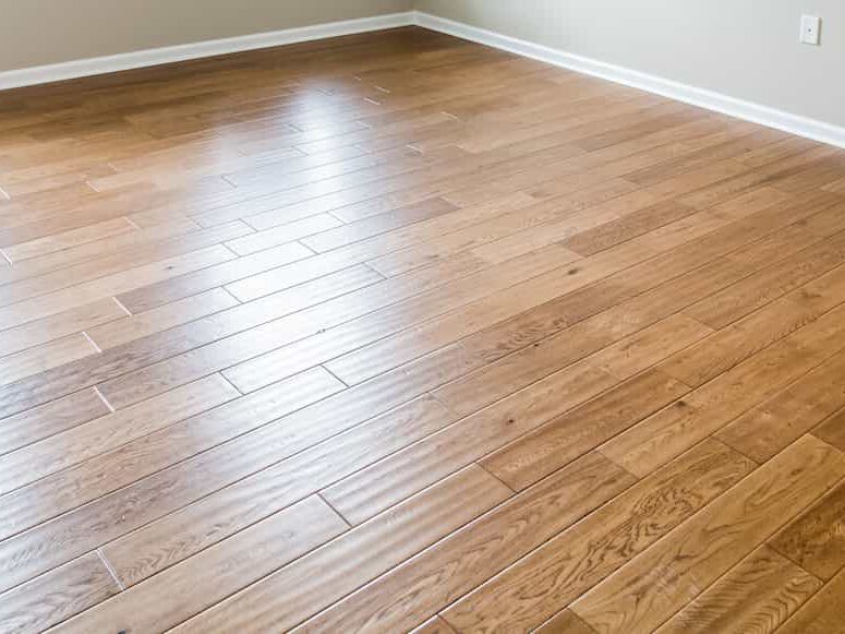 Empty room with light brown wooden plank flooring, white baseboards, and cream-colored walls. No furniture or decor is visible.