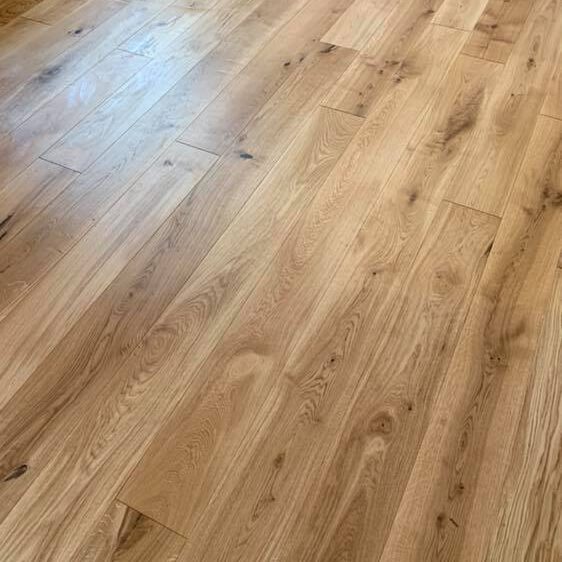 Close-up view of a clean wooden floor with natural grain patterns and knots. The planks are arranged lengthwise, showcasing a smooth finish and light brown, natural wood tones.